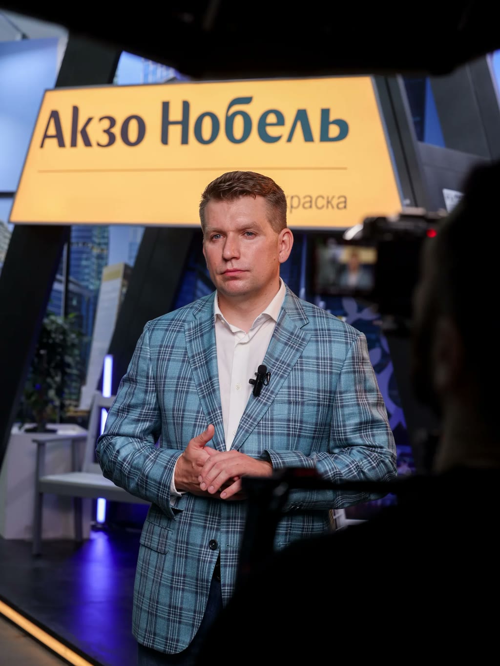Интервью на съёмке для «Акзо Нобель»: камера на переднем плане, спикер у стенда с логотипом — фильм о компании держится на людях в кадре